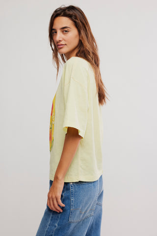 Woman wearing a light yellow t-shirt with a colorful graphic and blue jeans on a plain background