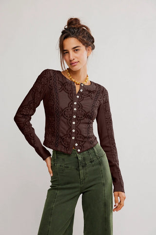 Woman wearing a brown lace top with buttons and green pants on a plain background