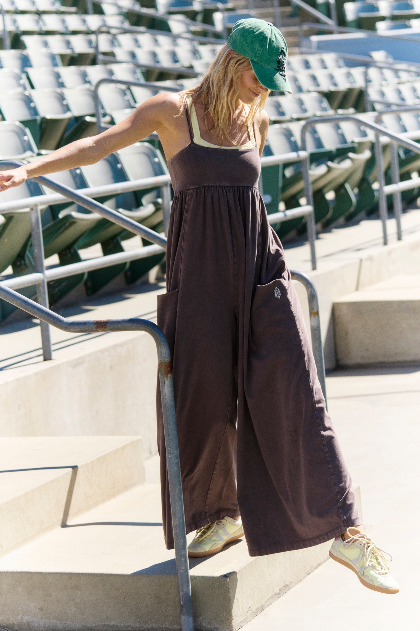 Woman in a brown romper and green cap standing on steps with stadium seats in the background