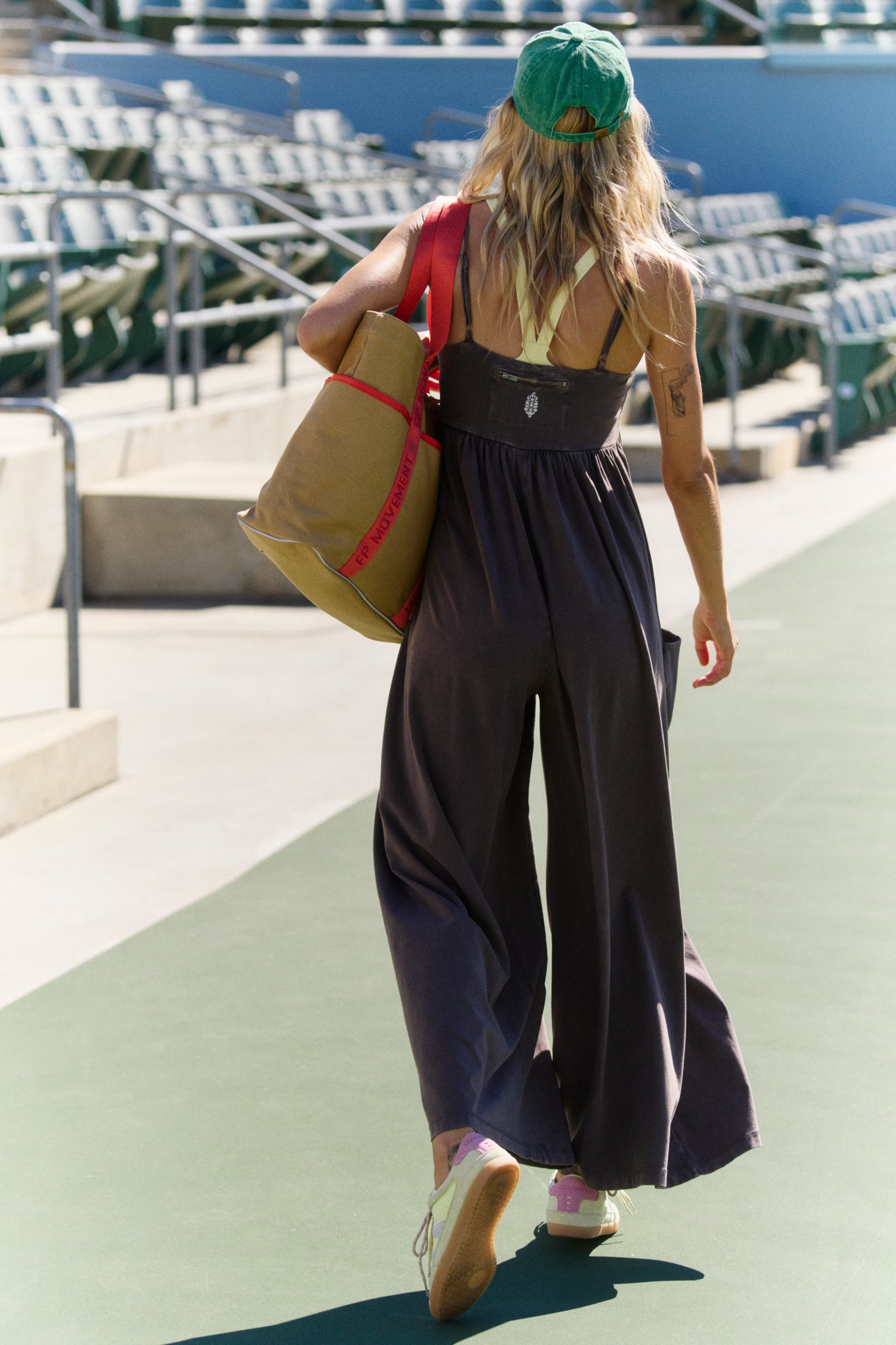 Person walking outdoors with a large beige bag, wearing a brown jumpsuit and green cap.