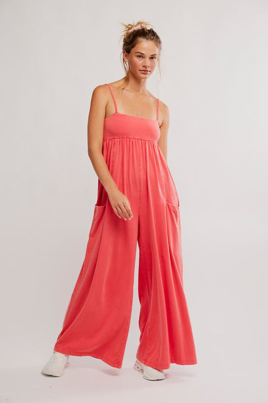 Woman wearing a coral jumpsuit on a light gray background