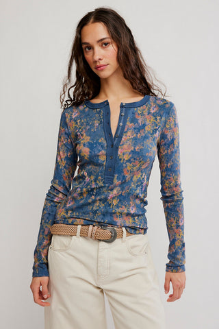 Woman wearing a blue floral long-sleeve top and white pants on a plain background