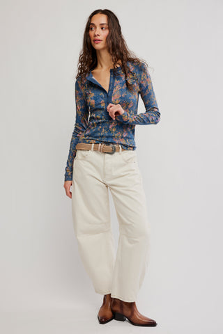 Woman wearing a blue floral blouse and white pants on a plain background