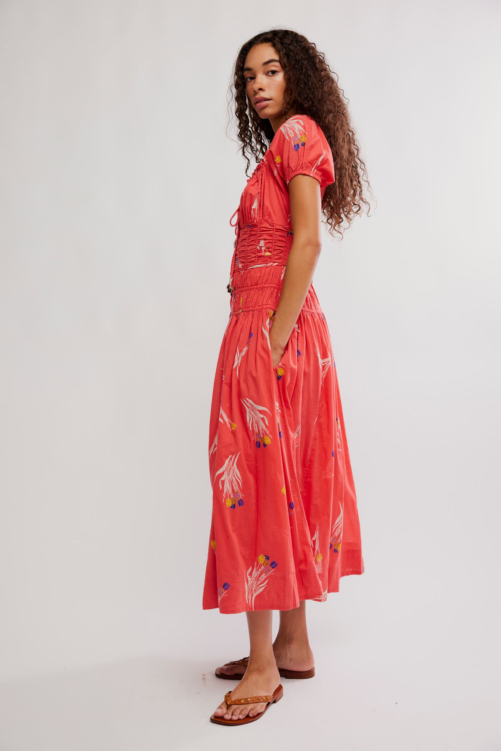 Woman wearing a coral dress with white floral patterns on a white background