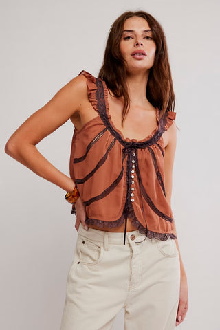 Woman wearing a brown sleeveless top with lace details and white pants on a plain background