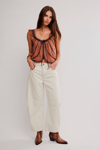 Woman wearing a brown top and white pants on a plain background