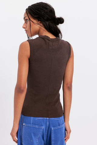 Person wearing a brown sleeveless top and blue pants on a white background