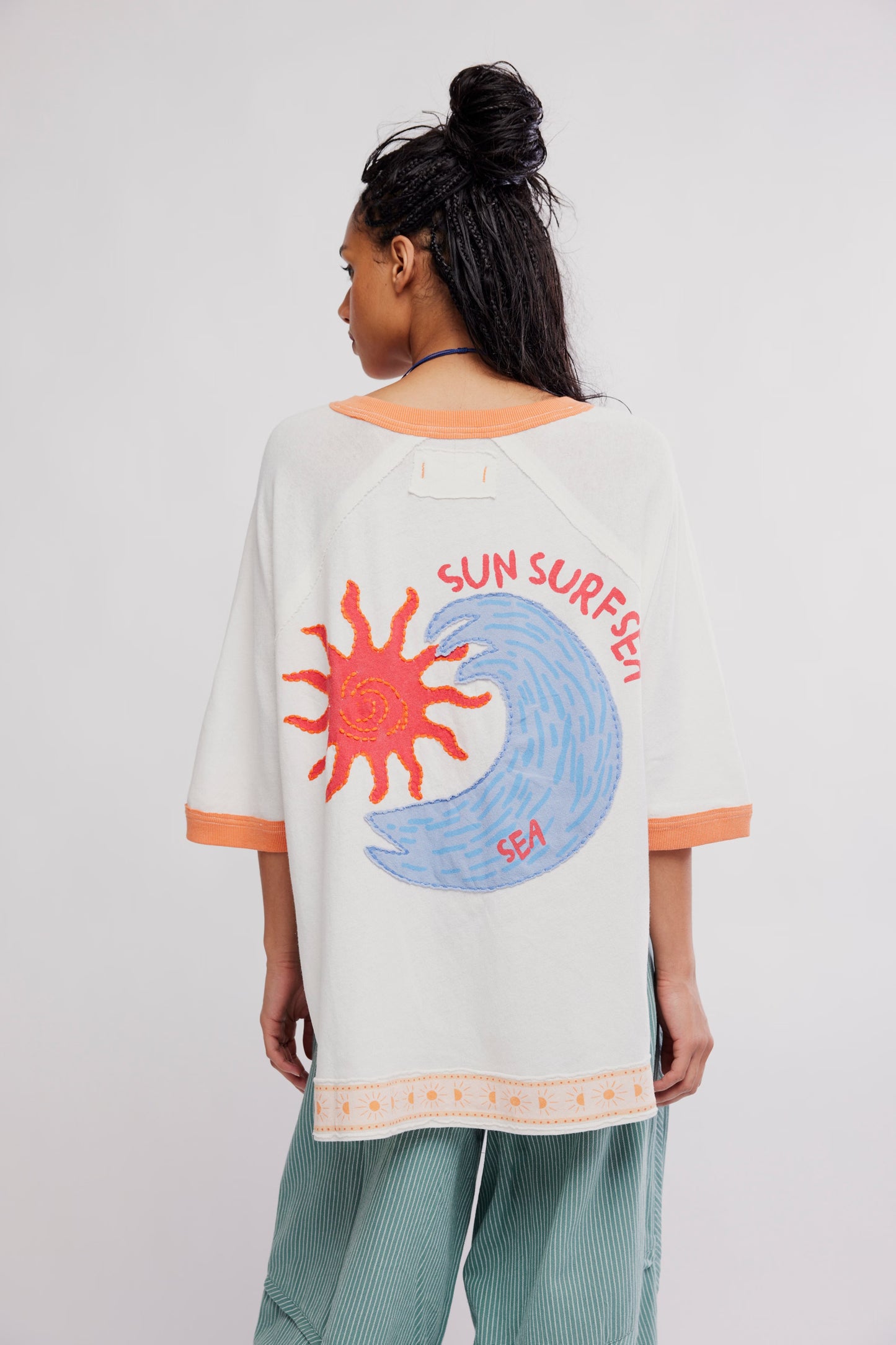 Person wearing a white t-shirt with a sun and wave design and 'Sun Surfer Sea' text on a plain background