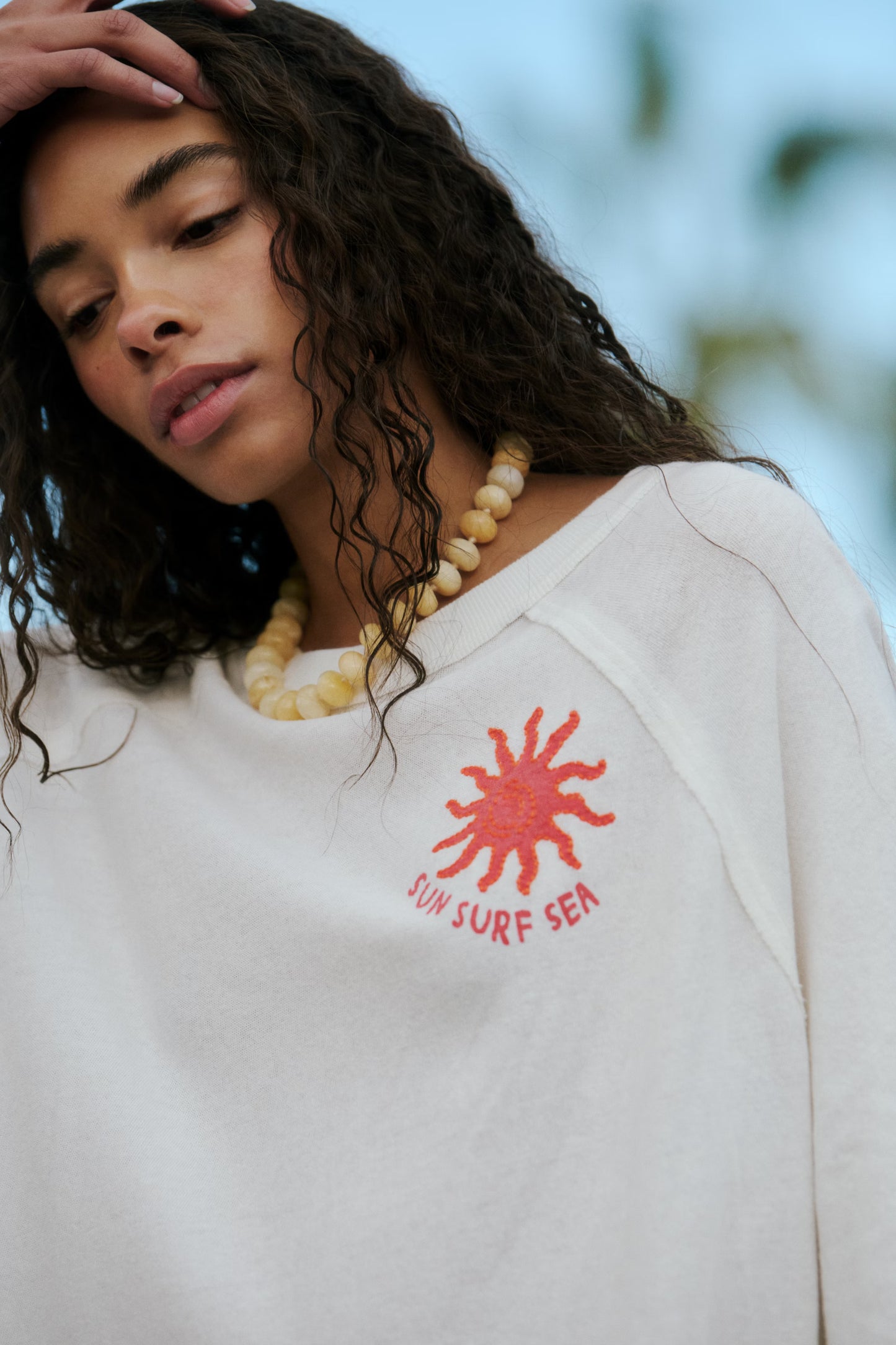 Person wearing a white sweatshirt with a red sun design and text, outdoors.