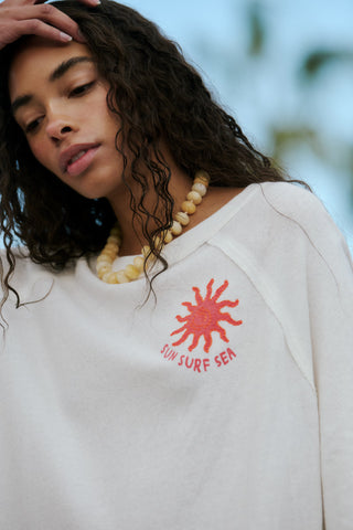 Person wearing a white sweatshirt with a red sun design and text, outdoors.
