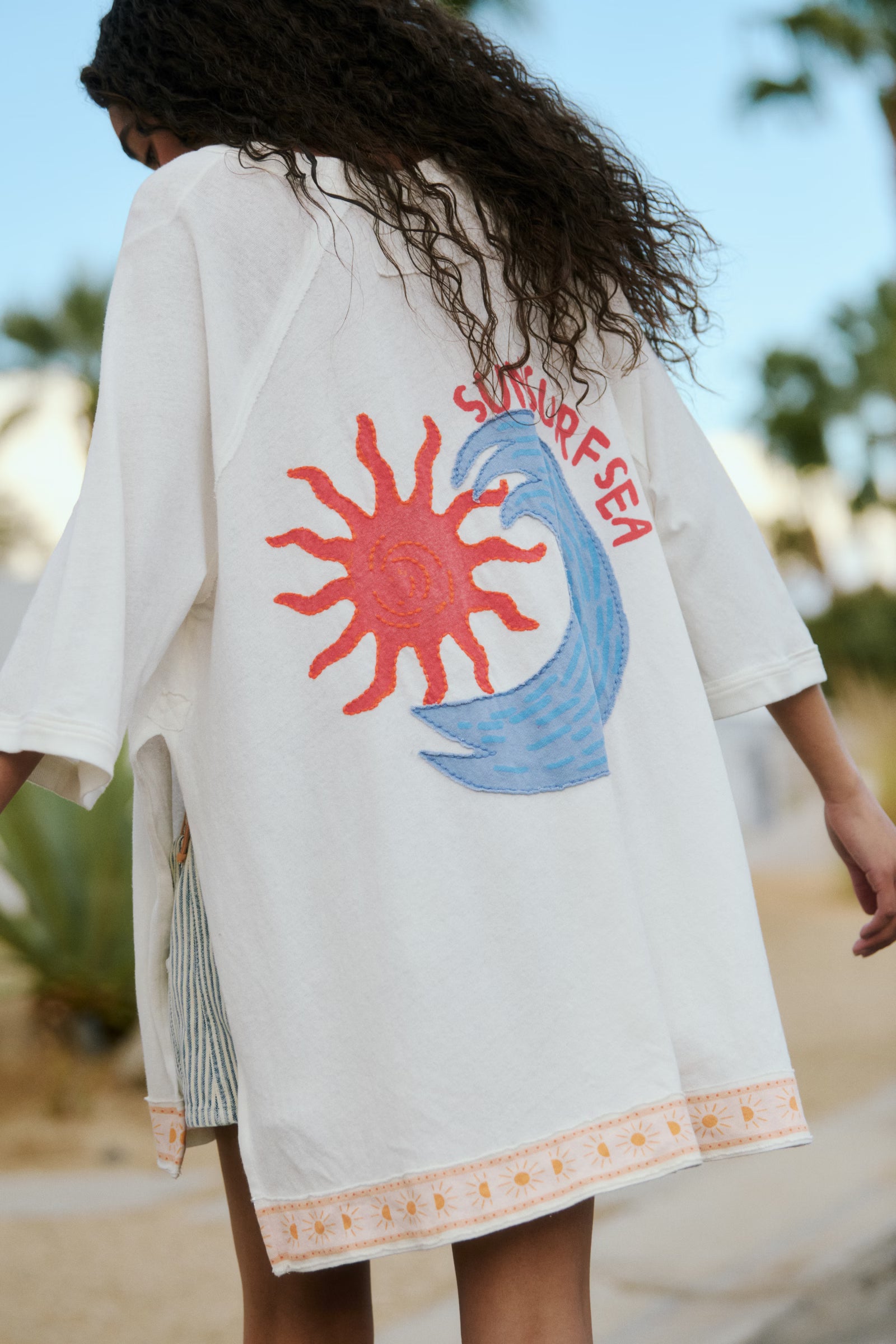 Person wearing a white kimono-style garment with a colorful graphic on the back, standing outdoors.