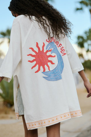 Person wearing a white kimono-style garment with a colorful graphic on the back, standing outdoors.