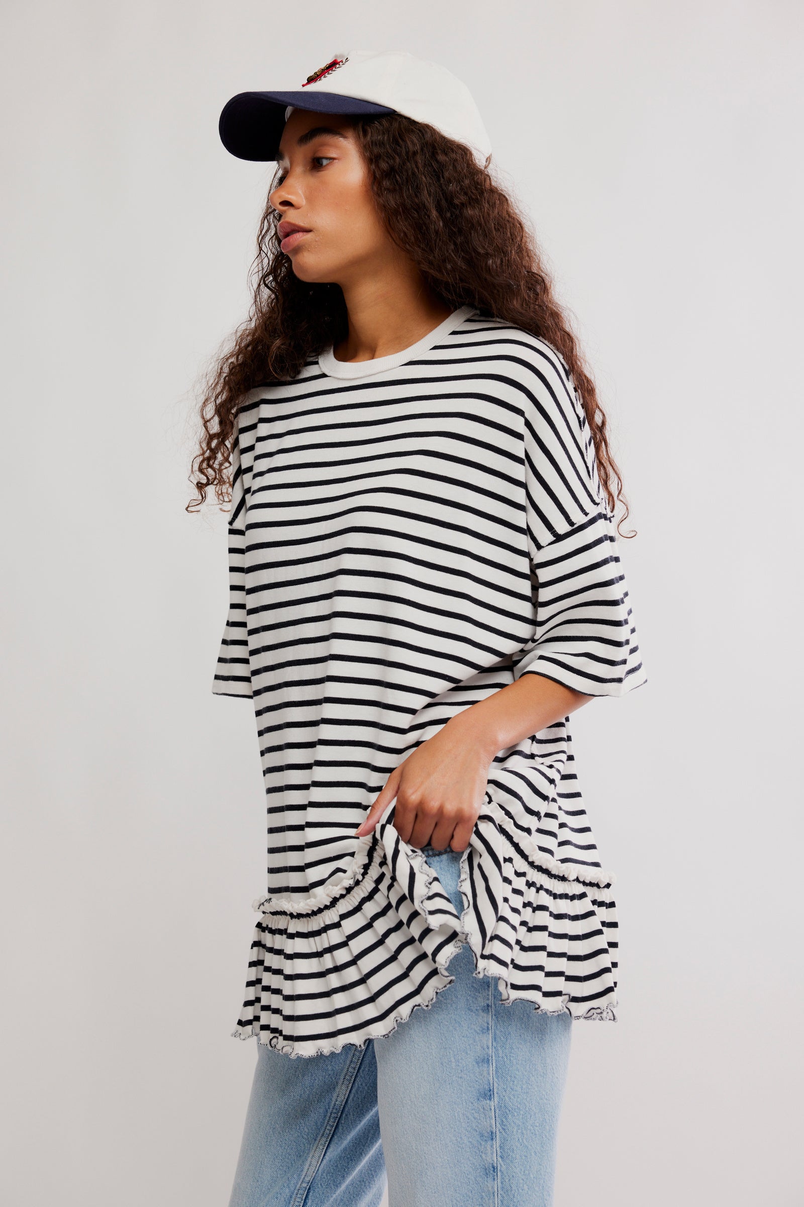 Woman wearing a black and white striped shirt with rolled-up sleeves and light blue jeans on a plain background