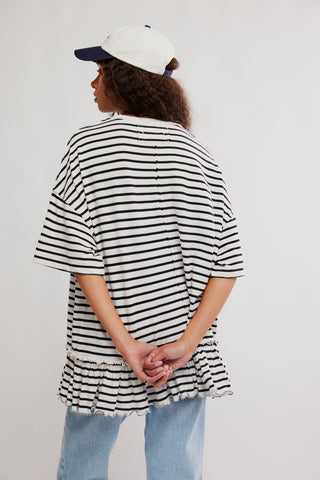 Person wearing a black and white striped shirt with ruffled hem on a plain background