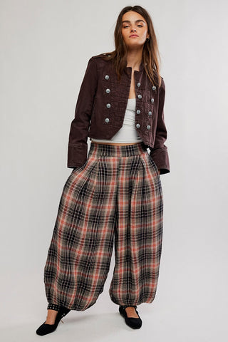 A model wearing a brown plaid jacket and matching wide-leg plaid trousers, paired with a white top and black shoes, set against a plain white background.