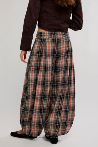 A person shown from the back wearing loose, wide-leg plaid pants in black, gray, and rust red, paired with a dark brown cropped top and black flats, against a light gray studio background.
