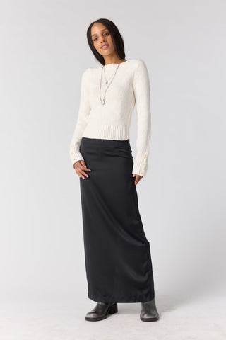 Women wearing a white sweater and black skirt against a neutral phot backdrop. 
