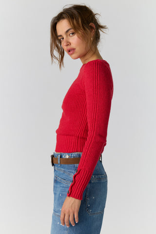 A woman wearing a bright red ribbed knit long-sleeve sweater and blue jeans, shown from the side against a plain light gray studio background.