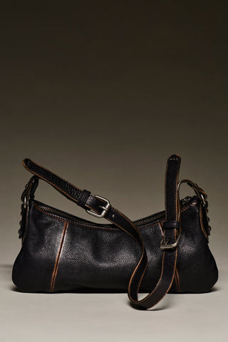 A black pebbled leather shoulder bag with a long strap, silver-tone hardware, and contrasting brown stitching, photographed against a dark gradient studio background.