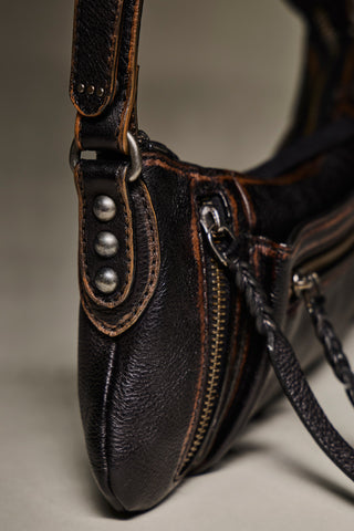 Close-up of a dark brown textured leather shoulder bag with silver-tone metal studs, a brass zipper, and contrast stitching on a neutral studio background.