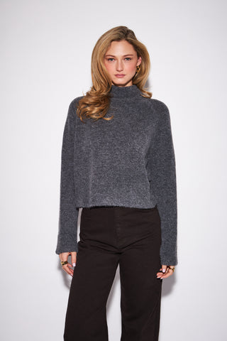 A woman modeling a dark gray fuzzy cropped mock-neck sweater with long sleeves, paired with black wide-leg pants, against a plain light gray background.