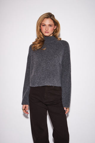 Woman wearing a gray turtleneck sweater and black pants on a white background