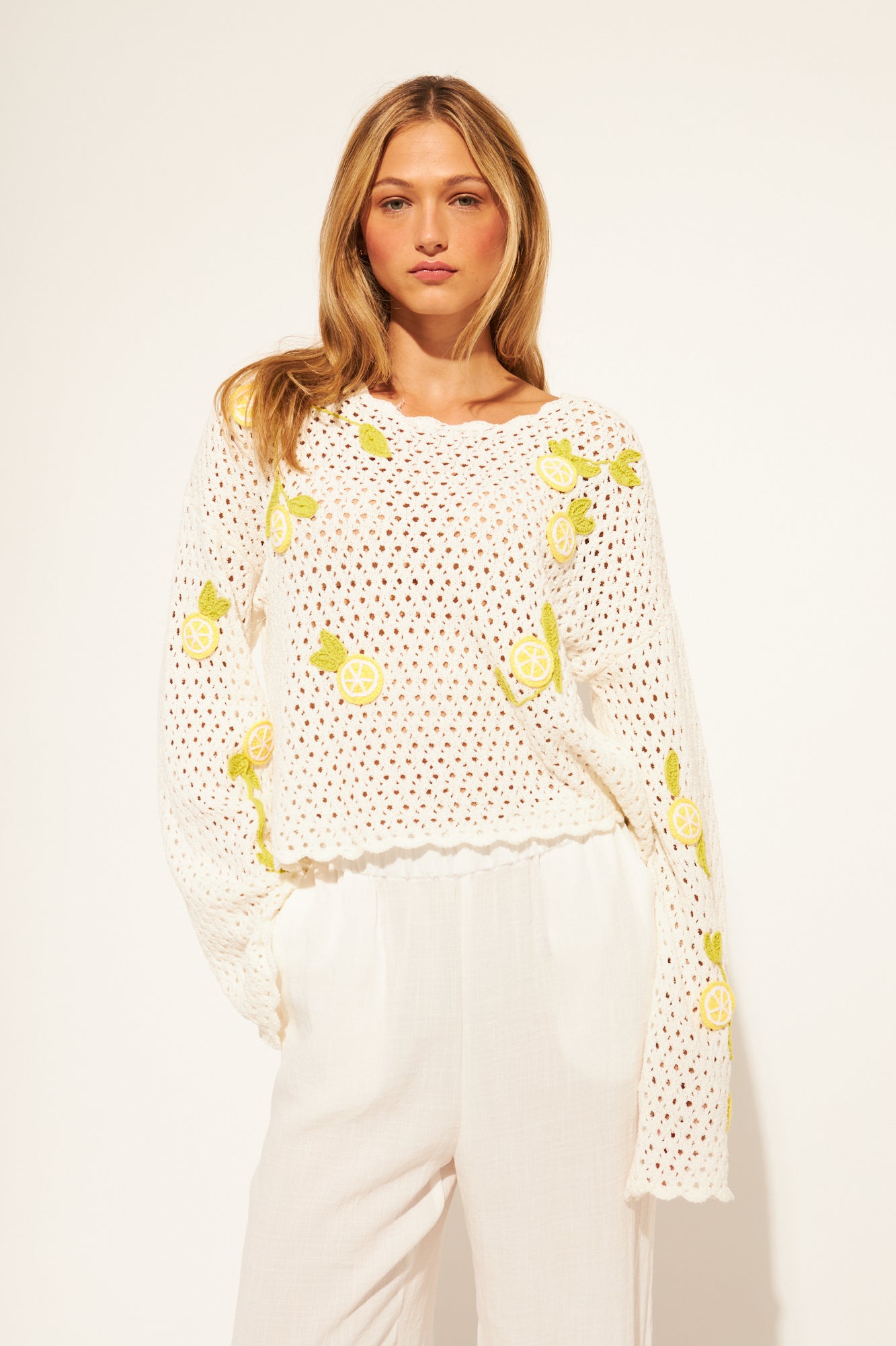 Woman wearing a white crochet sweater with yellow lemon designs on a plain background