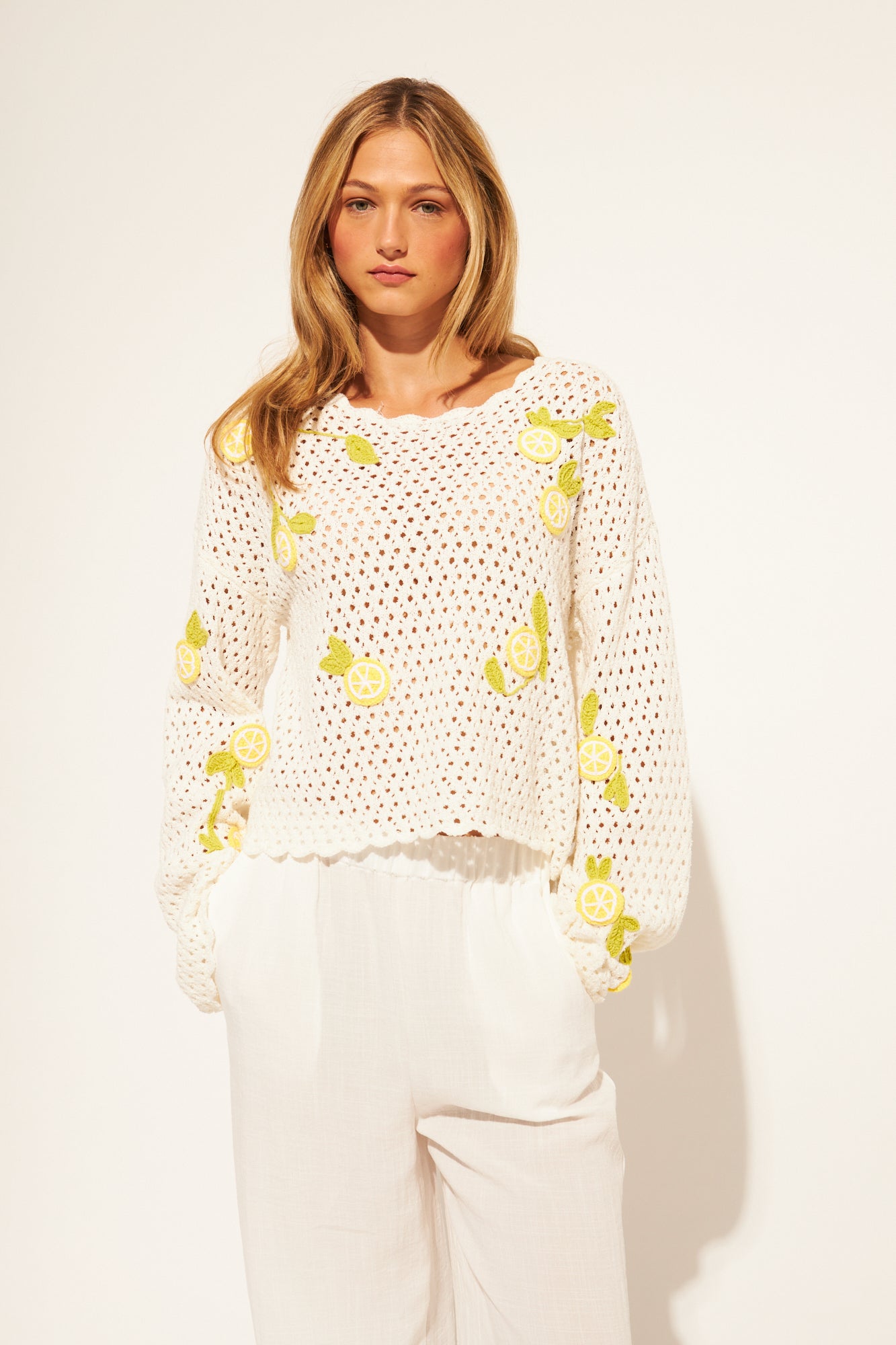 Woman wearing a white crochet top with yellow lemons patterns on a plain background