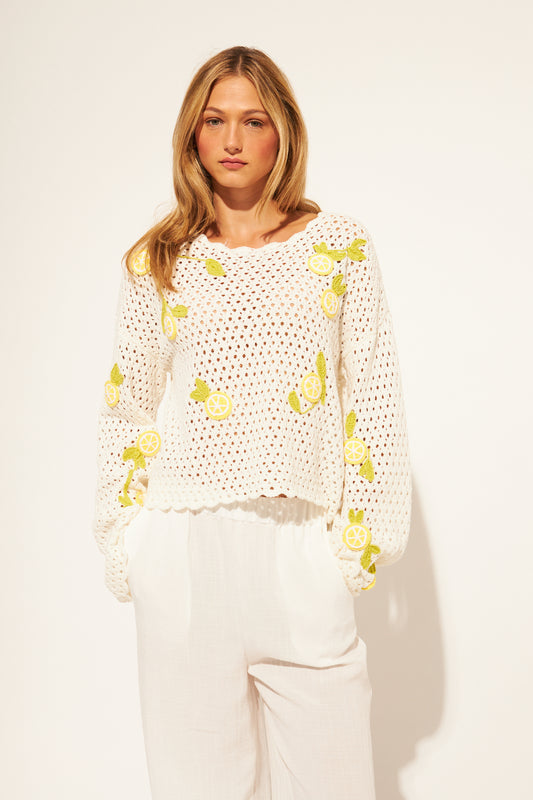 Woman wearing a white crochet top with yellow lemons patterns on a plain background