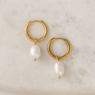 gold earrings with a pearl drop laying on a table