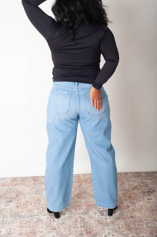 Person wearing light blue jeans and a black top on a plain background