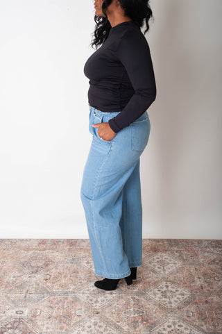 Person wearing light blue jeans and a black top standing on a patterned rug.