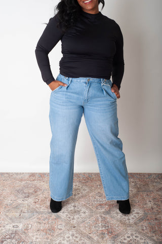 Person wearing light blue jeans and a black top on a neutral background