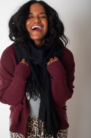 Woman wearing a maroon sweater, black scarf, and leopard print pants against a plain background