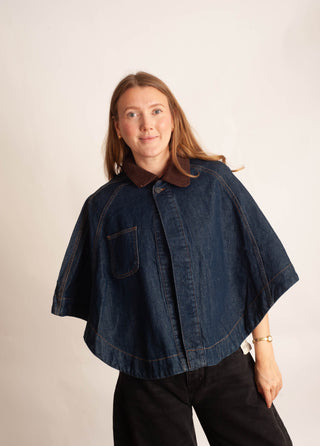 Women wearing a denim cape jacket with a cord collar against a neutral photo back drop. 