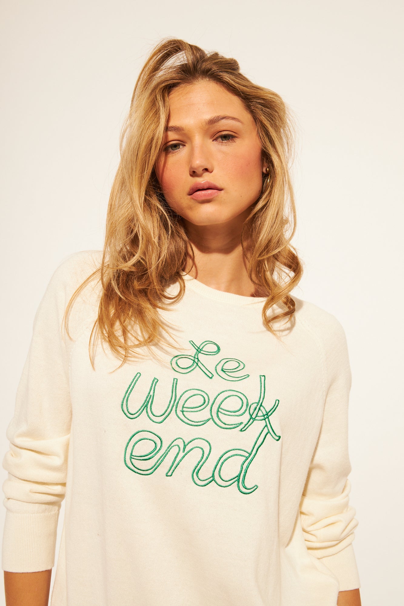 Woman wearing a white sweater with green text on a plain background