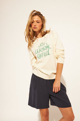 Woman wearing a white sweatshirt with green text and black shorts on a white background