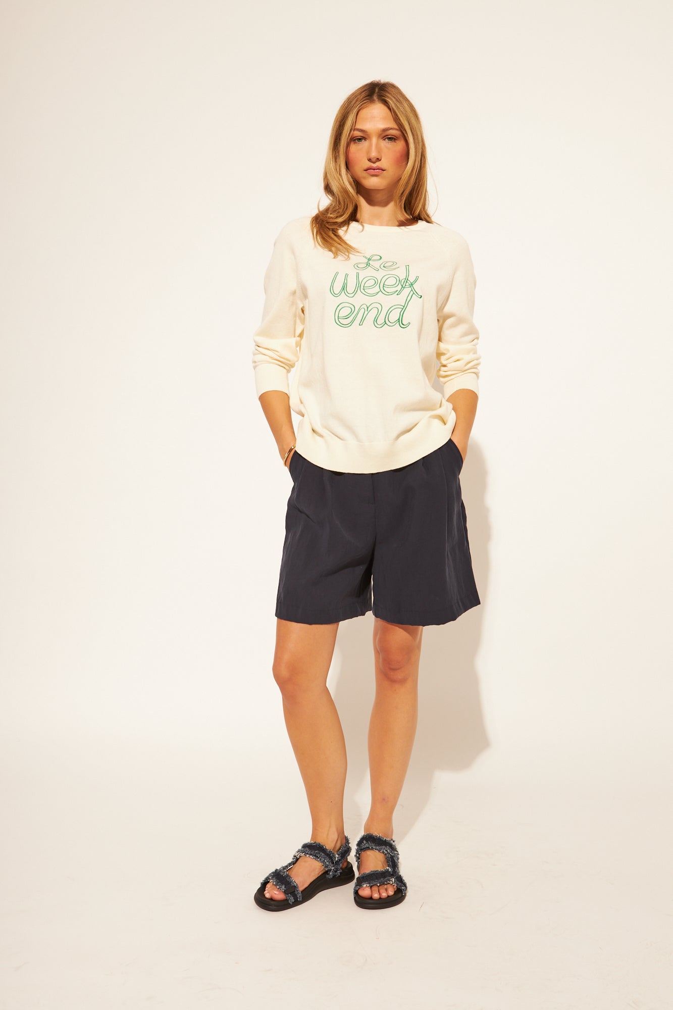 Person wearing a beige sweatshirt with text and navy shorts on a white background