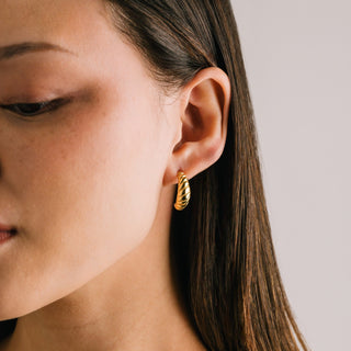 A person wearing a gold-colored hoop earring.