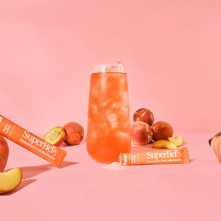 SuperBelly drink mix with peach slices on a pink background