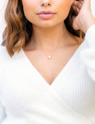 Woman wearing a delicate necklace with a small pendant against a white background