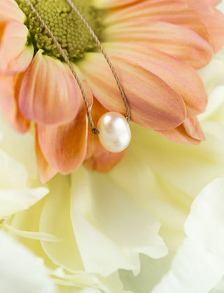 Pearl necklace draped over a pink flower with a soft focus background