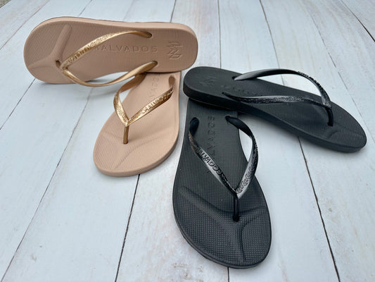 Two pairs of sandals, one beige and one black, on a light wooden floor.