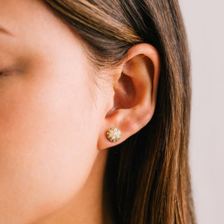 person wearing a pair of floral earrings with gemstones on a beige background