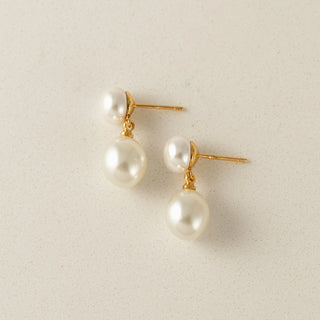 Pair of pearl earrings with gold posts on a light beige background