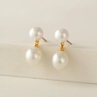 Pair of pearl earrings with gold accents on a light beige background
