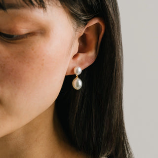 Close-up of a person wearing pearl earrings with a neutral background
