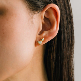 Close-up of an ear wearing gold heart-shaped earrings with a neutral background
