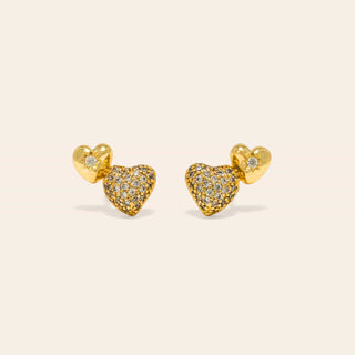 Heart-shaped gold earrings with diamond accents on a beige background