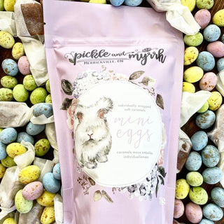 Pouch of 'Pickle and Myrhh' mini eggs surrounded by colorful Easter eggs.